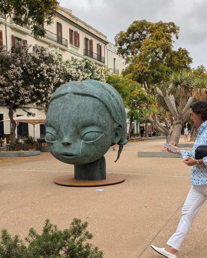 A large, modern sculpture of a child's head, an example of stunning street art in an urban square.