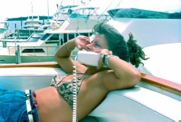 A woman on a boat uses a retro corded telephone, capturing the unique weirdness of 80s tech.