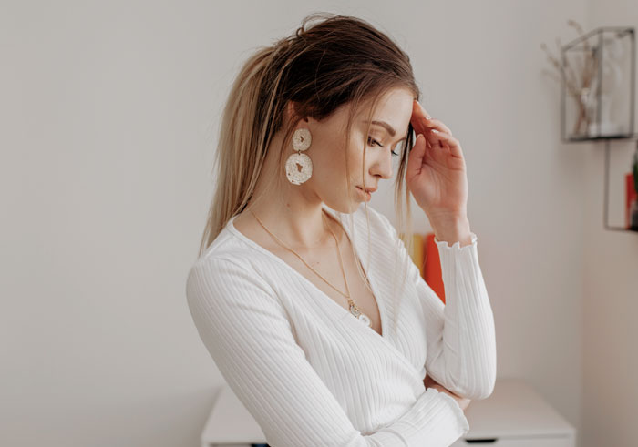 A woman looking down, with her hand on her head, representing relationship headaches.