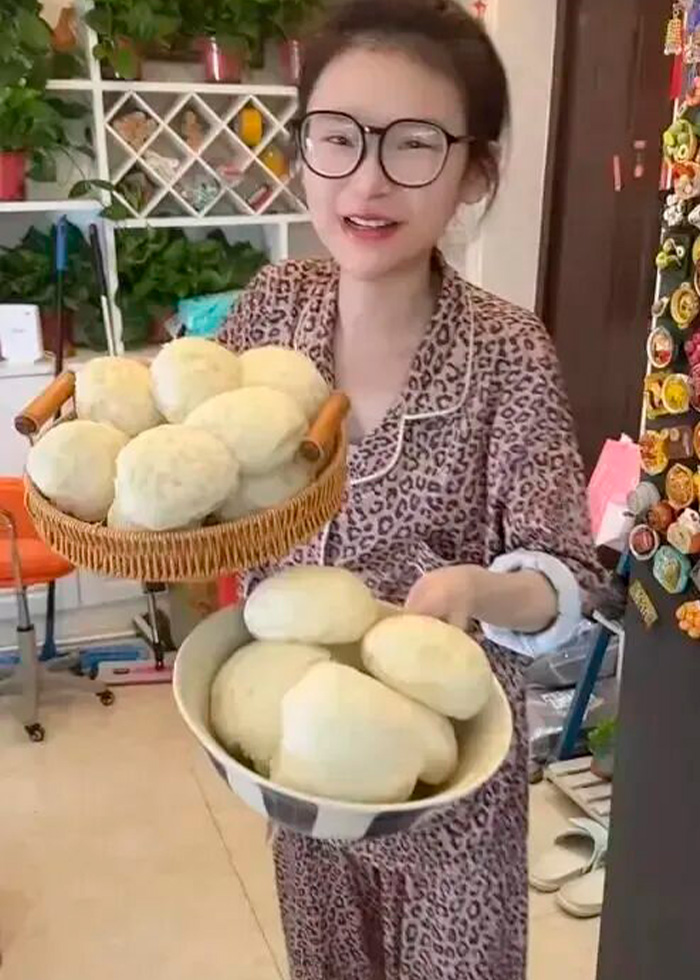 A mukbang star holding two baskets of bread, smiling at the camera, linking extreme eating to a dangerous condition.