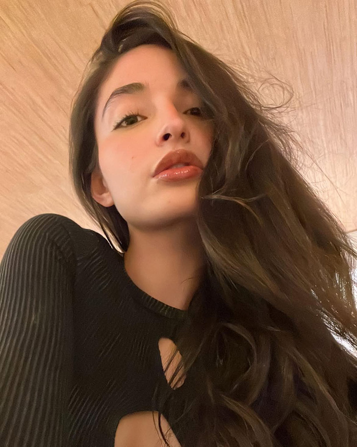 Emily Willis, the paralyzed actress, in a selfie from below, showcasing her deep brown hair and a black outfit, her family reveals her conscious locked-in state.