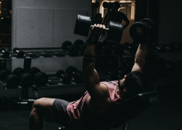 Man performing heavy dumbbell chest press, showing intense gym workouts that can impact men's private parts