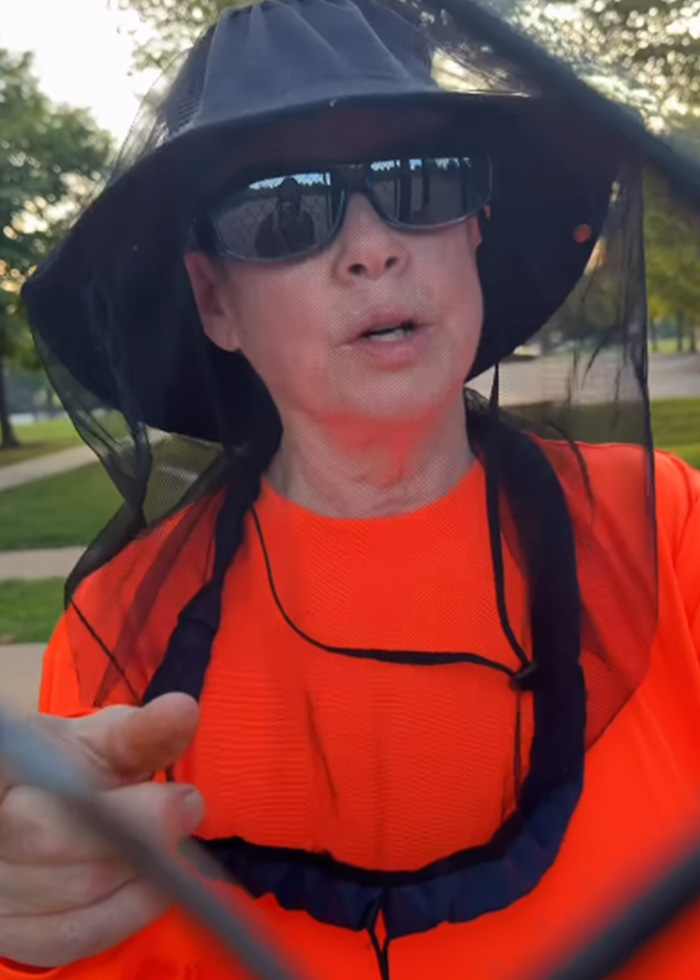 Woman wearing orange shirt and hat with netting speaking behind fence Woman wearing orange shirt and hat with netting speaking behind fence