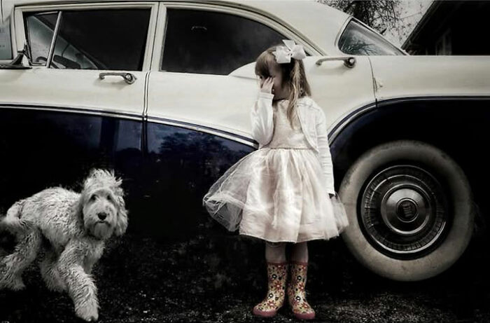 Street photo by Taylor Coble of a young girl and a dog in front of a vintage car.