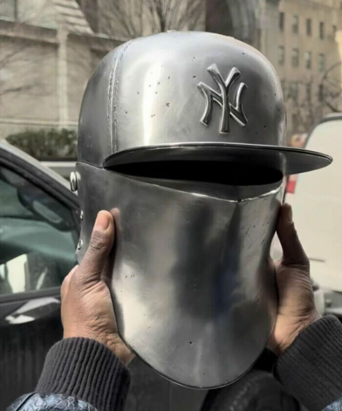 Unhinged image of a person holding a custom medieval helmet with a modern baseball cap brim and Yankees logo.