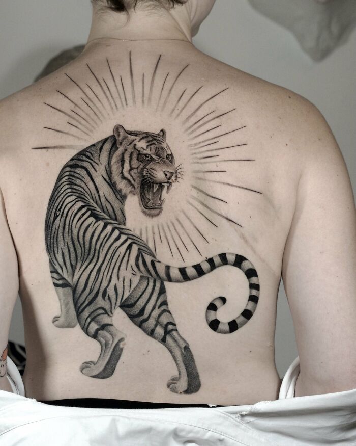 Realistic tiger tattoo with glowing rays on upper back nature ink tattoo