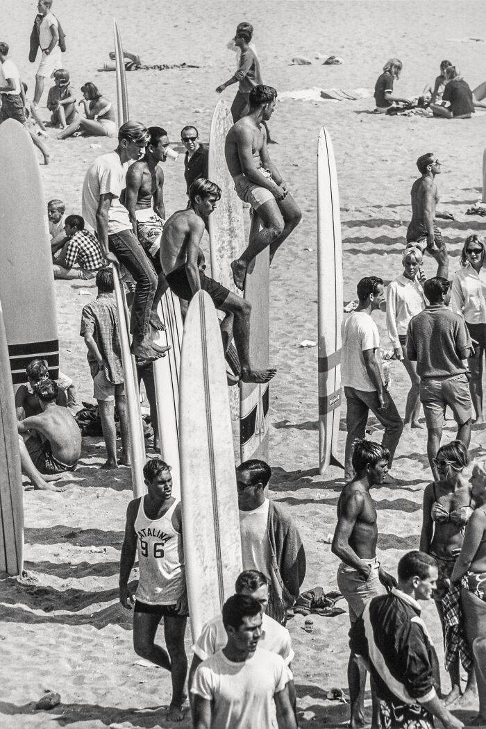 A crowded beach scene with surfers and their boards in this candid old photo, showing a slice of life generations ago.