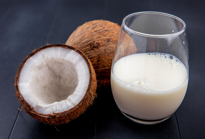 Two coconuts, one halved, next to a glass of coconut milk, evoking simple childhood beliefs about nature.