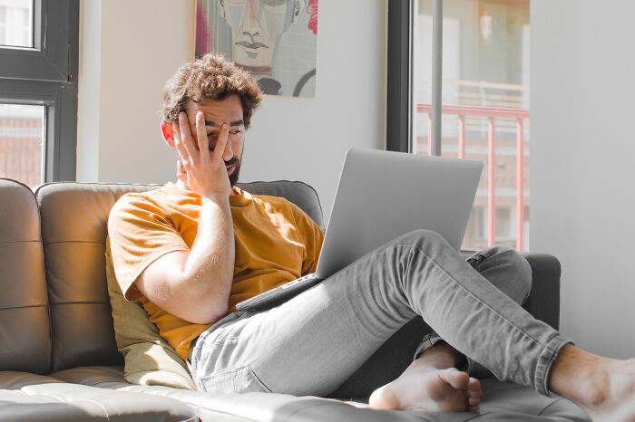 A man looking tired while using a laptop, representing dumb ways people ruin their lives.