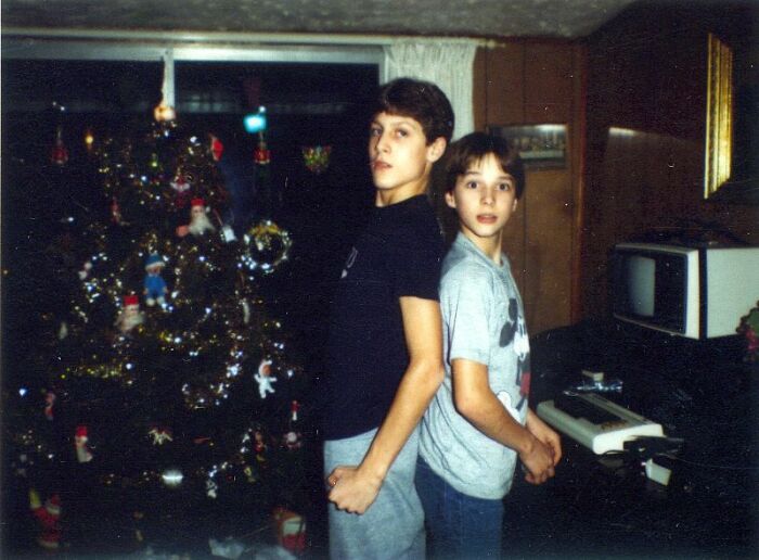 Two boys standing by a Christmas tree, with retro tech visible, illustrating 80s life.