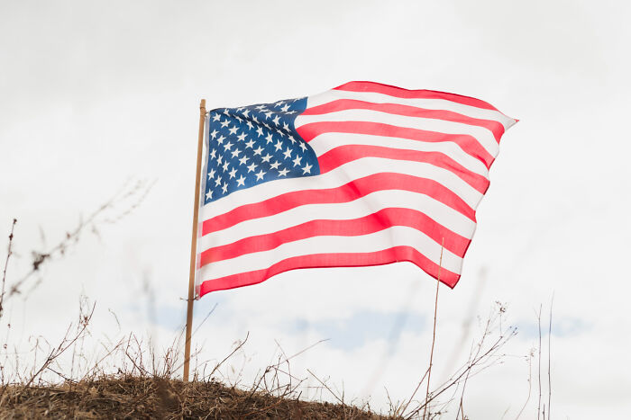 American flag waving in the wind against a cloudy sky, representing society's problems.