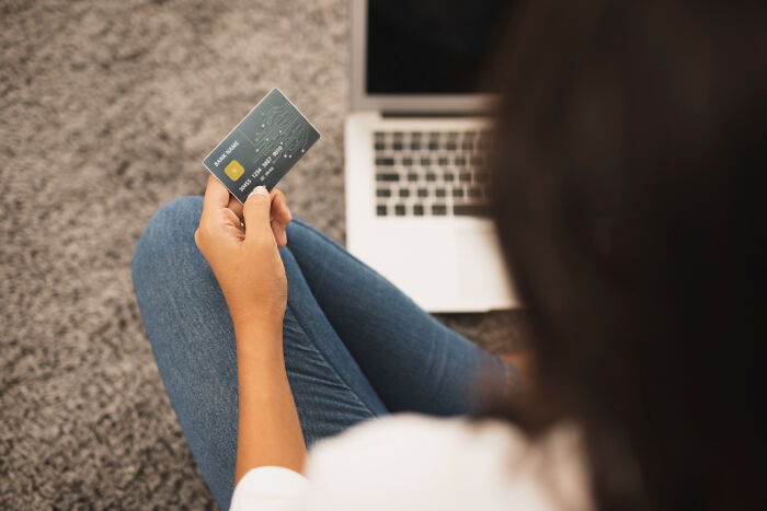 A person holding a credit card while sitting in front of a laptop