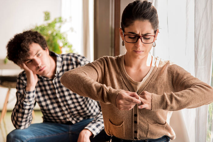 A woman taking off a ring while a man looks sad in the background, showing dumb ways people ruin their lives.