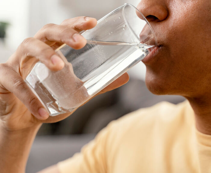 A person drinking water from a clear glass, highlighting potential problems with resource access in society.