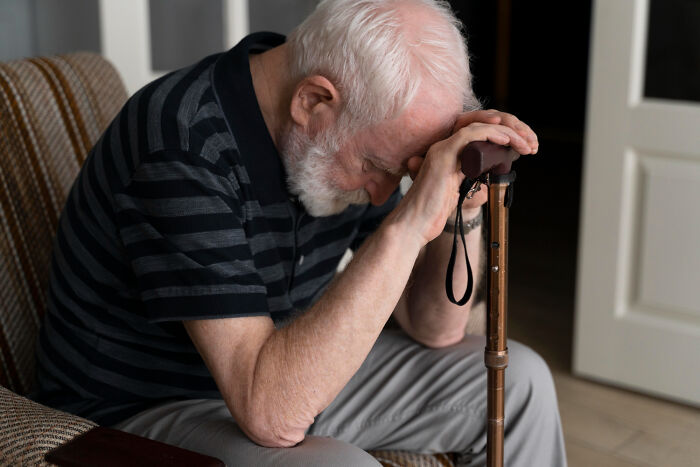 An elderly man with a walking stick, head down, looking sad, representing the problems society faces.
