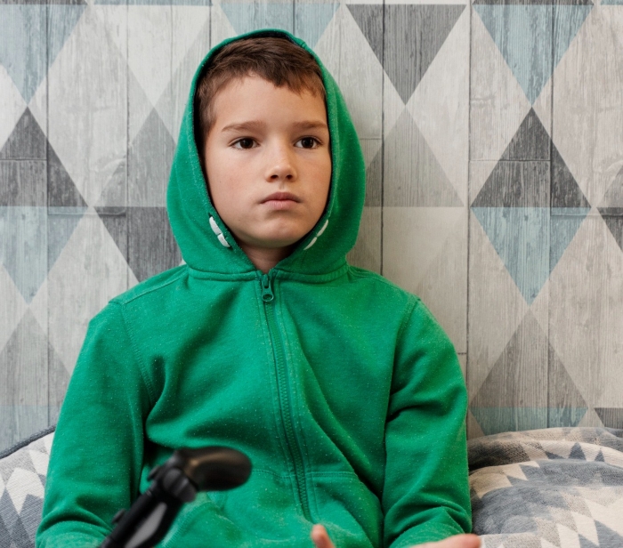 Boy in green hoodie looking serious indoors