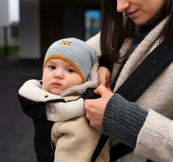 A woman adjusts a baby carrier, a common thing people do that others judge them for.