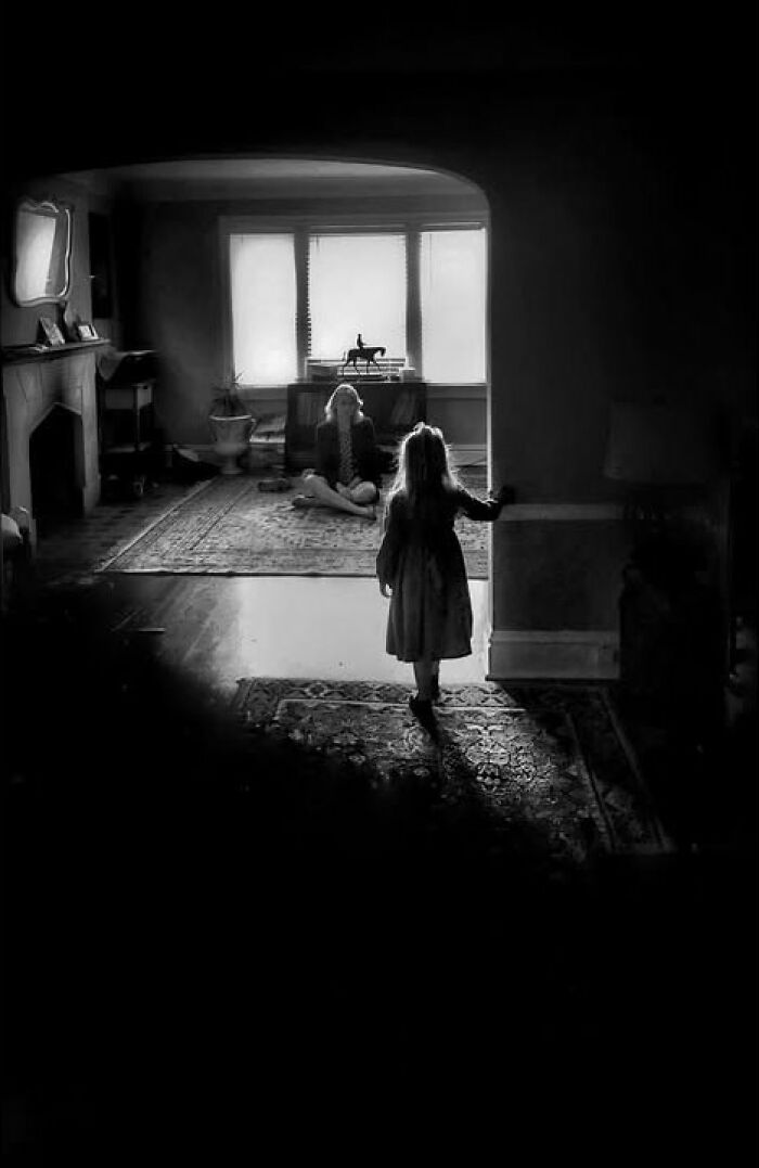 Taylor Coble street photo of a child walking into a brightly lit room where a woman sits by a window.