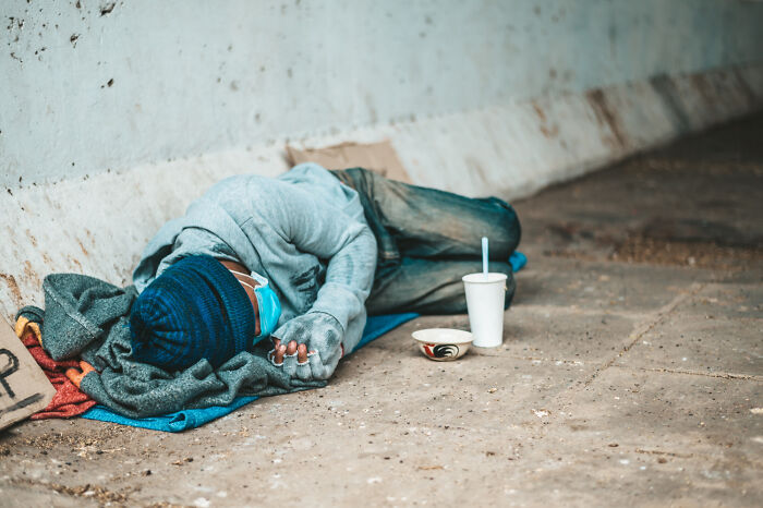 A homeless person sleeping on a mat with a cup and bowl, symbolizing the biggest problems society could face.