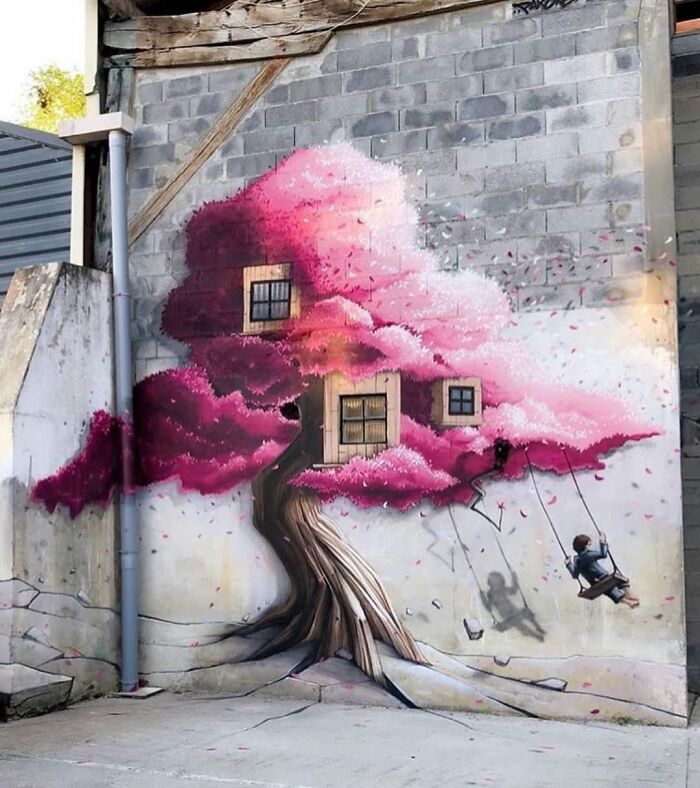 A vibrant pink cherry blossom street art mural on a building, featuring tiny windows and a child on a swing.
