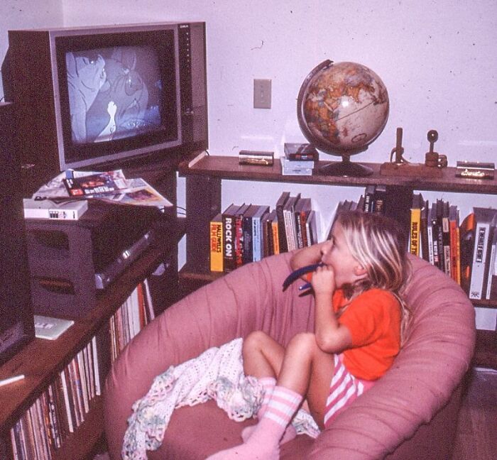 A young girl in a bean bag chair watching TV, surrounded by retro tech and a vintage globe.