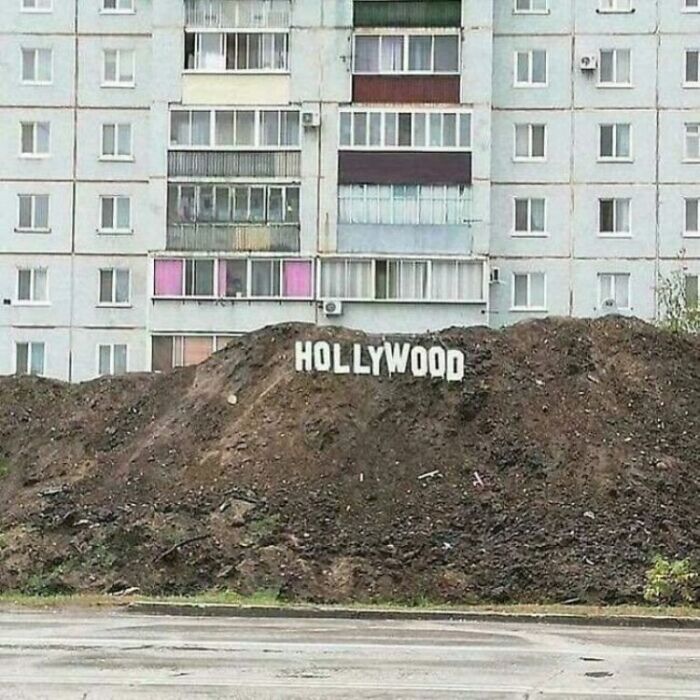 An unhinged image of a Hollywood sign on a dirt mound in front of an apartment building.
