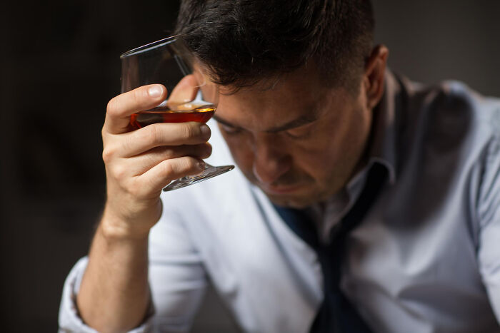 A man with a pensive expression, holding a glass of amber liquid, contemplating an unexpected end.