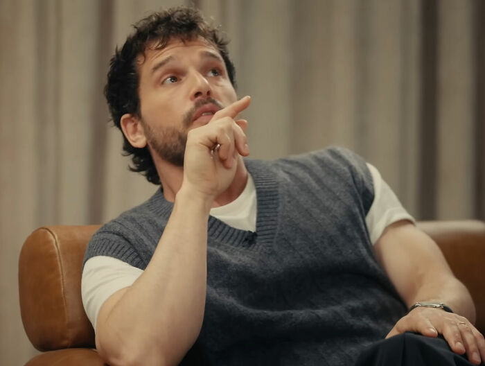 Actor from Game Of Thrones in casual sweater vest and white shirt indoors