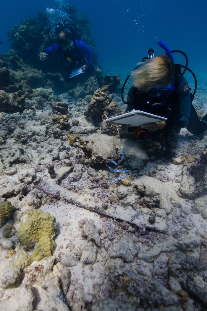 Two marine researchers surveying and measuring a shipwreck site discovered at the bottom of the ocean