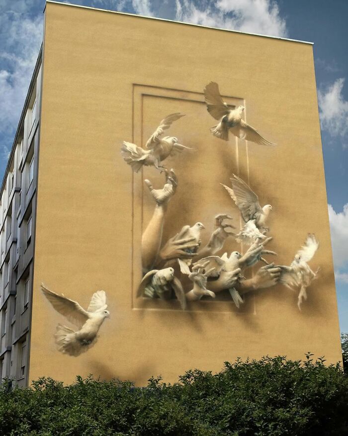 A stunning 3D street art mural of doves flying out of a wall, with hands reaching out to them.