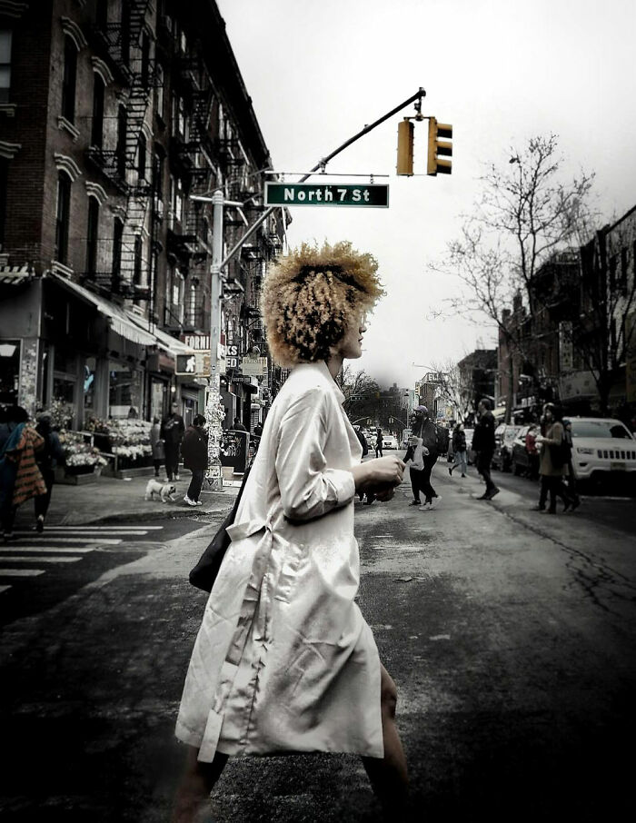 A striking street photo by Taylor Coble of a woman with curly hair walking across a city street with buildings.