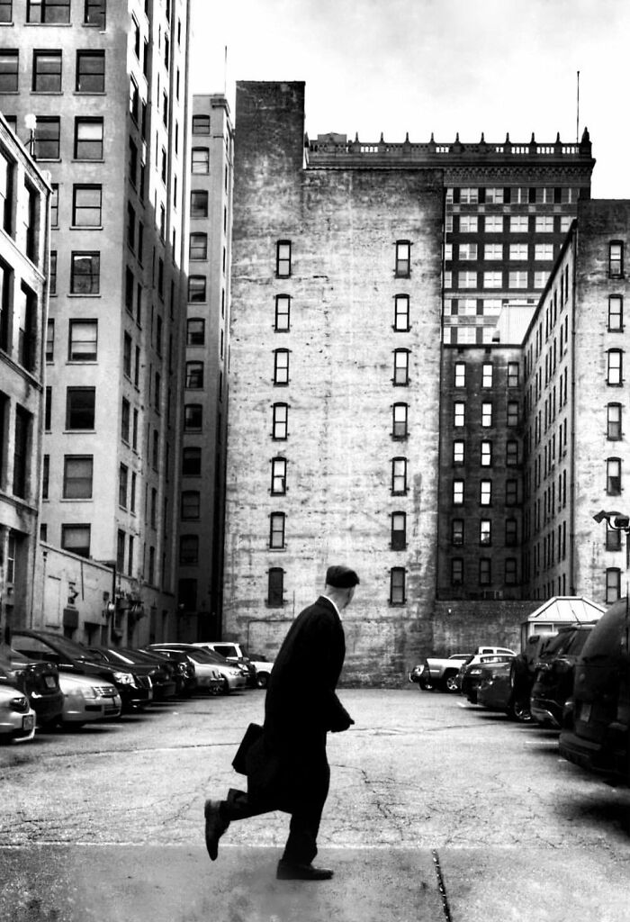 Black and white street photo by Taylor Coble capturing a man hurrying through a city parking lot.