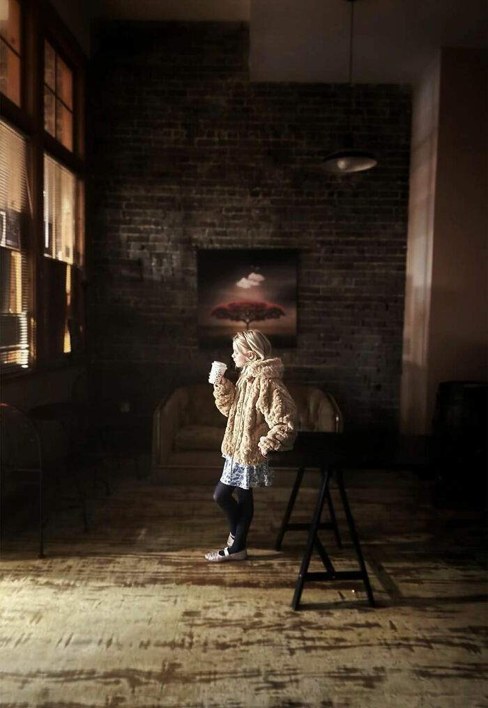 A child in a cozy coat sips a drink in a rustic room, a fleeting moment captured in a compelling street photo.