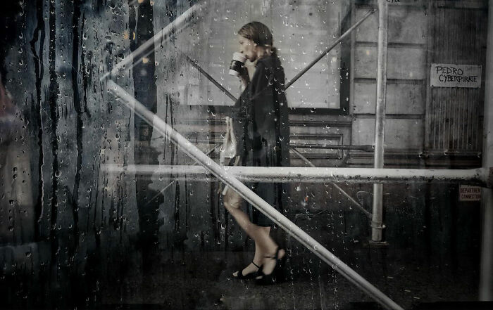 A woman walks in the rain, seen through a water-streaked window, a captivating street photo by Taylor Coble.