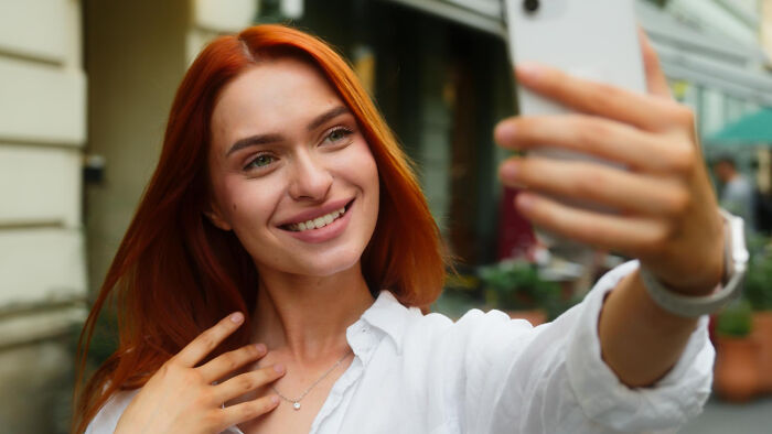 A young woman with red hair taking a selfie, reflecting on future societal problems.