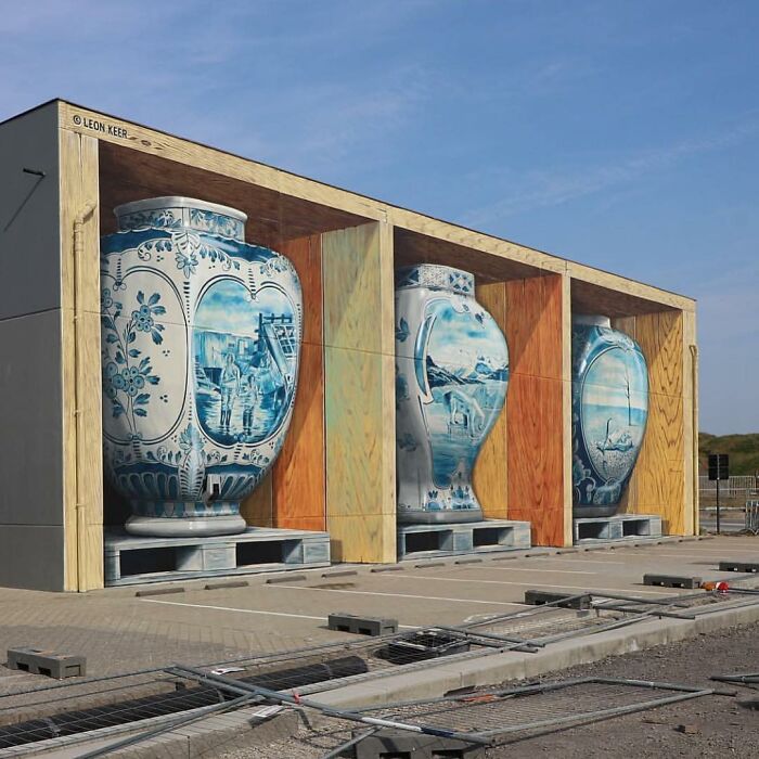 An optical illusion street art mural depicting three large blue and white vases stored inside wooden shelves.