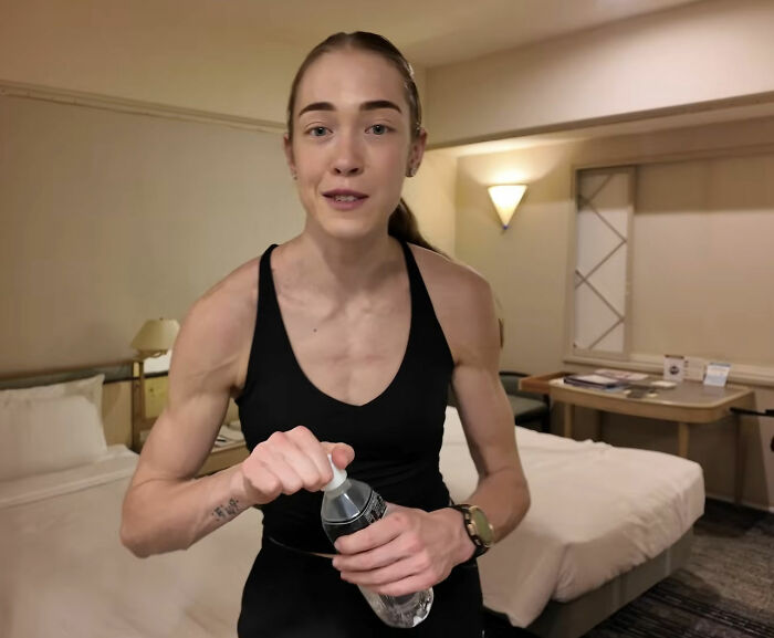 HYROX athlete opens a water bottle in a hotel room, looking fit and ready for a race.