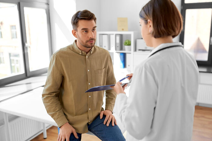 A male patient sits on an exam table listening to a female doctor during a medical exam. Patients often tell lies.