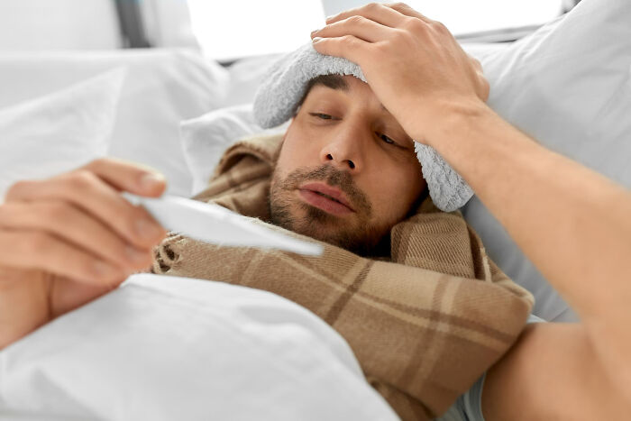 A sick man with a thermometer, highlighting dumb ways people ruin their lives through poor health.