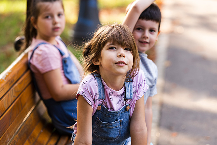 Two young girls and a boy, half-siblings, in foster care. A girl looks up, while another sits on a bench.