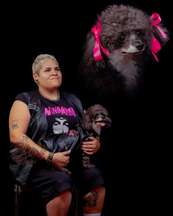A person with tattoos holding their pet dog, dressed in matching leather outfits, with a portrait of the dog above on a black background, for silly portraits of pets and their owners.
