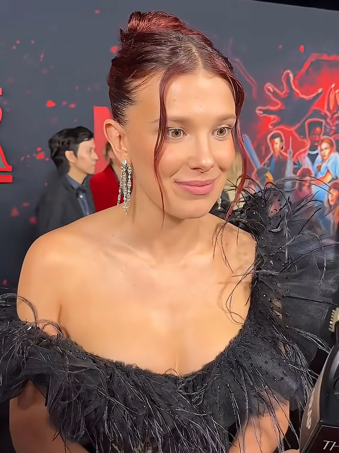 Millie Bobby Brown smiling at an event, part of Hollywood secrets and famous faces.