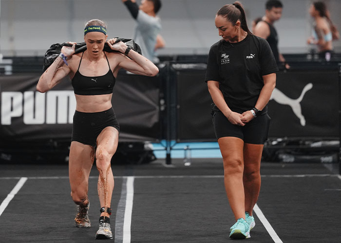 HYROX athlete with soiled shorts, continuing a race alongside an official after the incident.