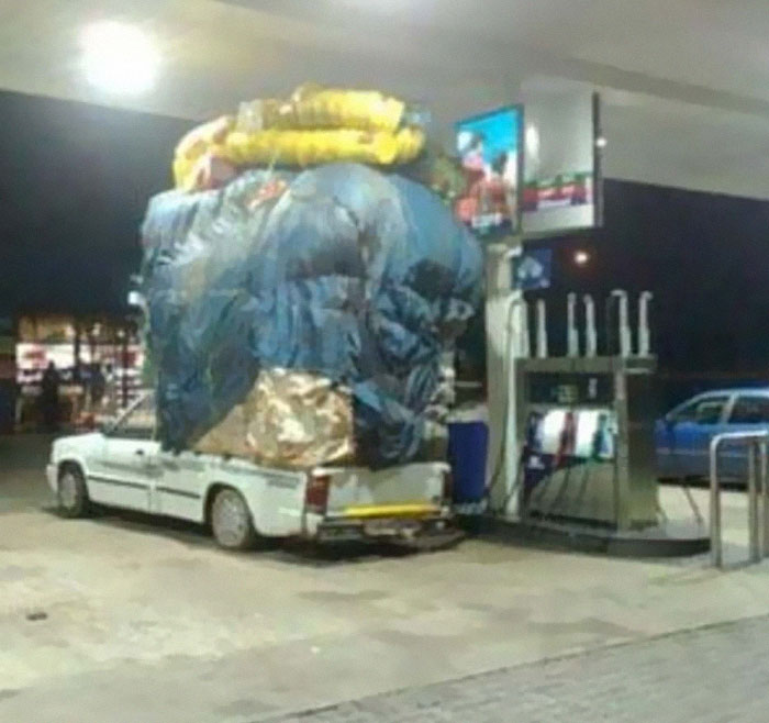 Car heavily overloaded with large items covered in tarp at gas station in moving fails pics