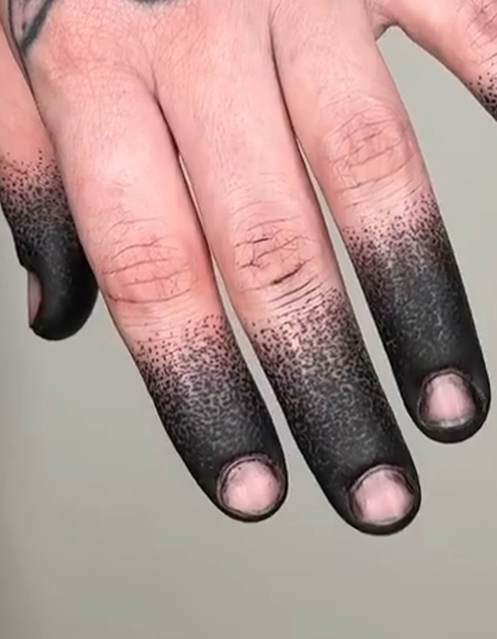 A close-up of a hand with the viral fingertip tattoo trend featuring black stippled ink. A close-up of a hand with the viral fingertip tattoo trend featuring black stippled ink.