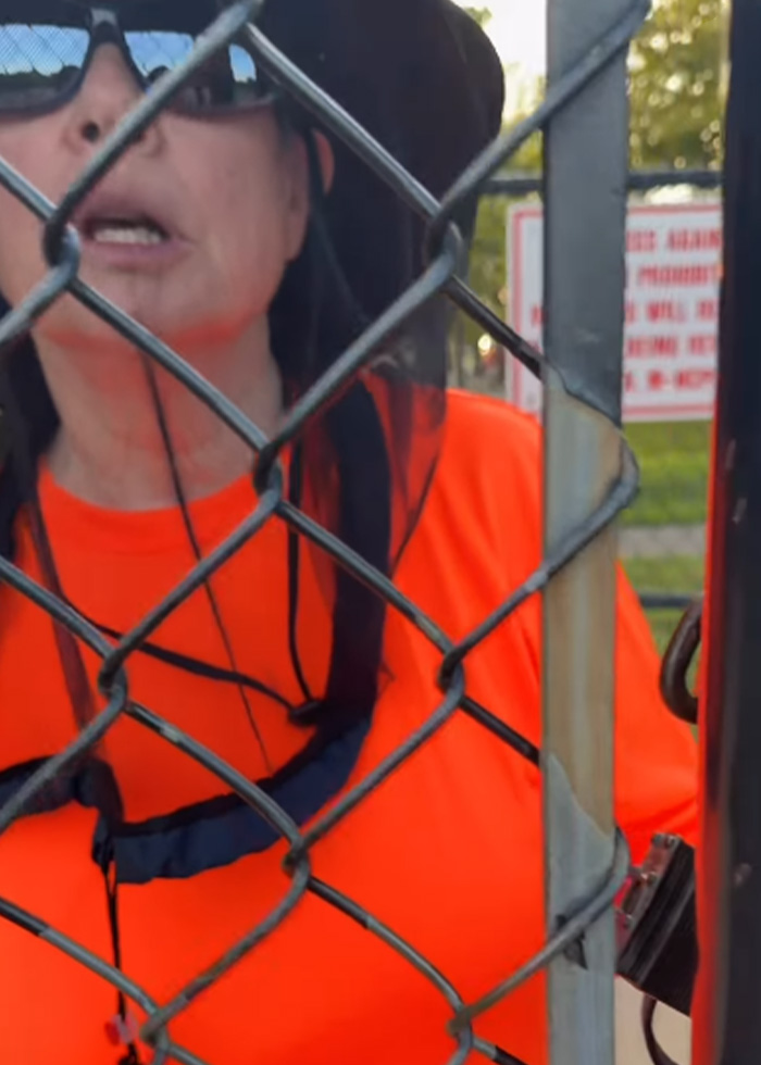 Woman in orange shirt behind chain-link field gate Woman in orange shirt behind chain-link field gate