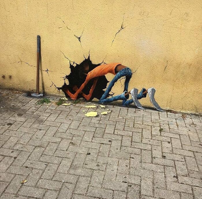 Street art of a person crawling through a hole in a yellow wall, showcasing creative street art.