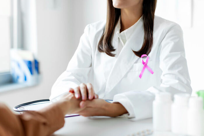 A doctor wearing a pink ribbon holding hands with a patient, demonstrating support for arguments heard in court.