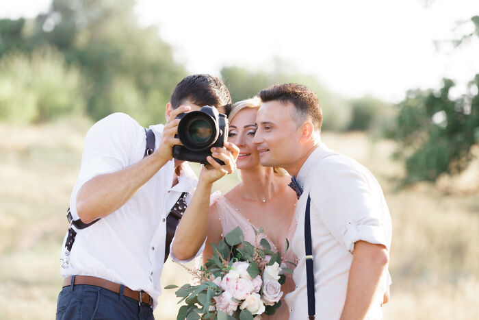 A wedding photographer showing the camera screen to a newlywed couple in a field