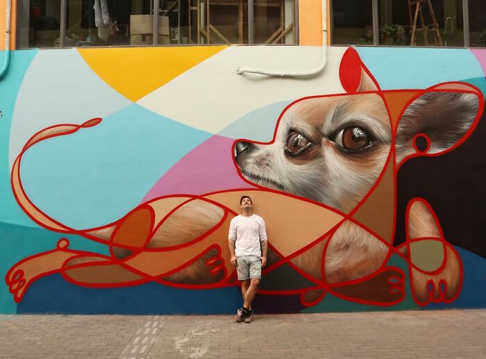 Man standing in front of a colorful street art mural of a chihuahua dog.